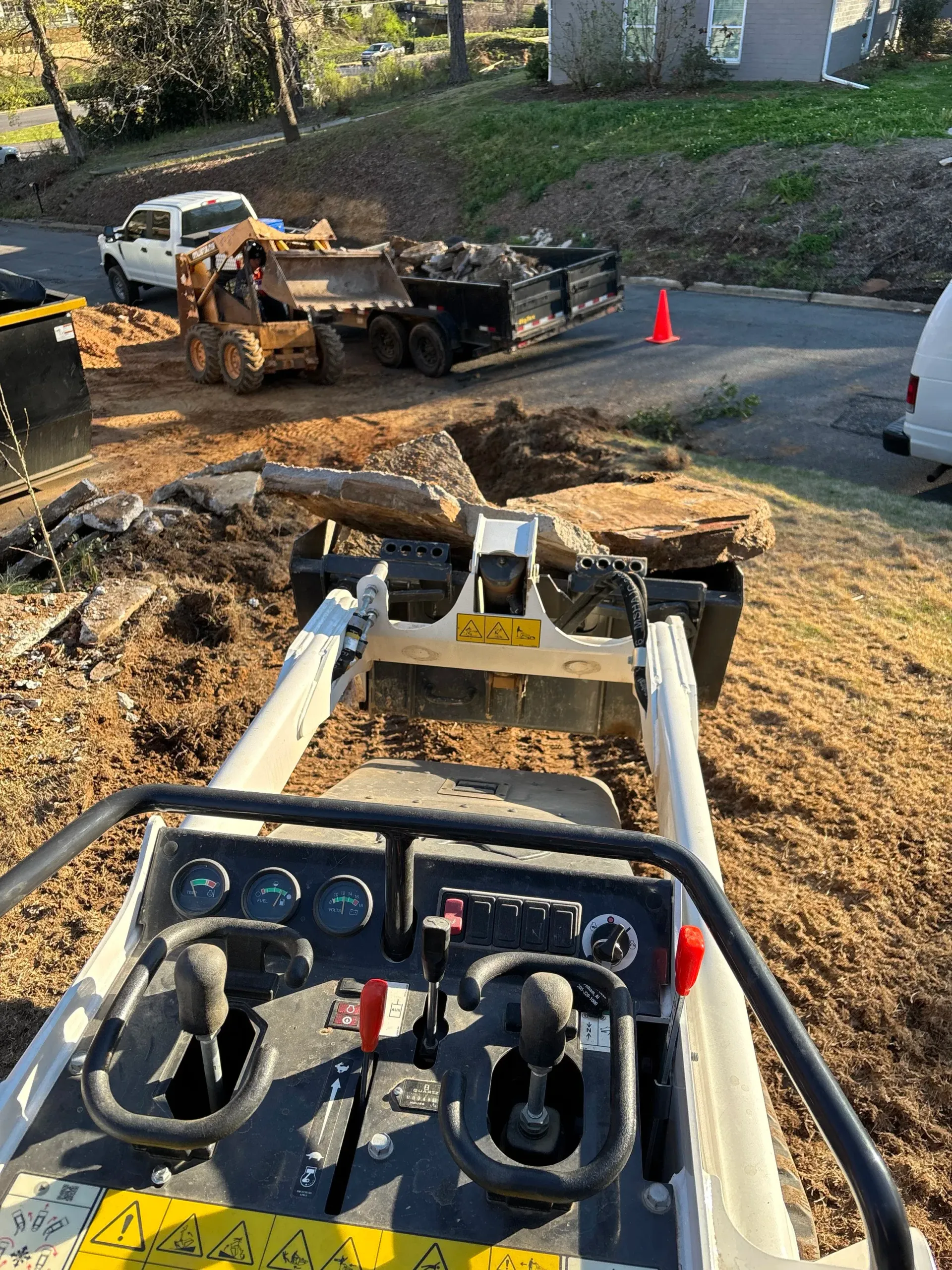 A small construction vehicle operating near a dirt pile, with a truck and loader in the background.
