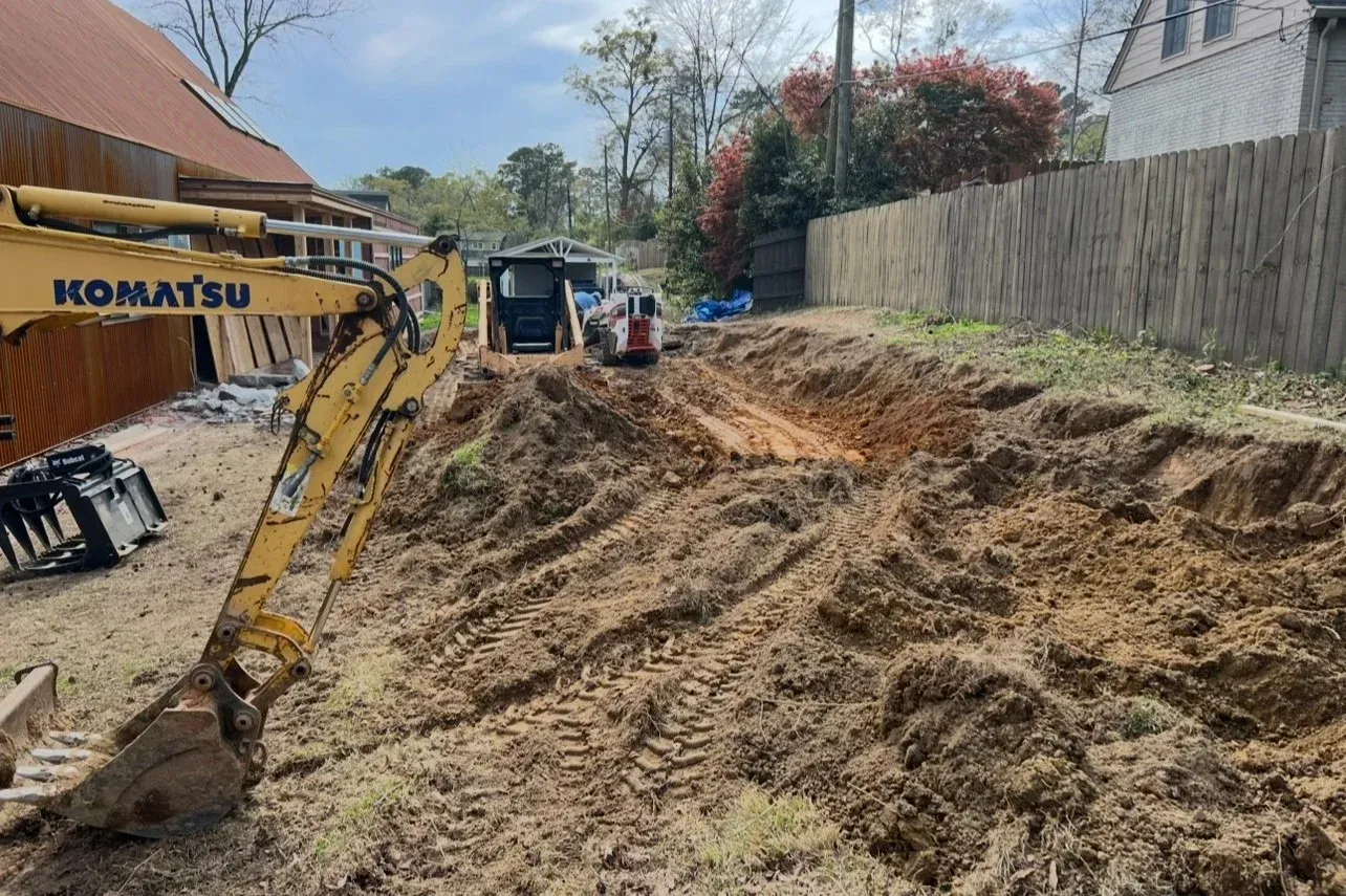 Yellow Komatsu excavator digging in a dirt yard, with two small excavators, near a wooden fence.
