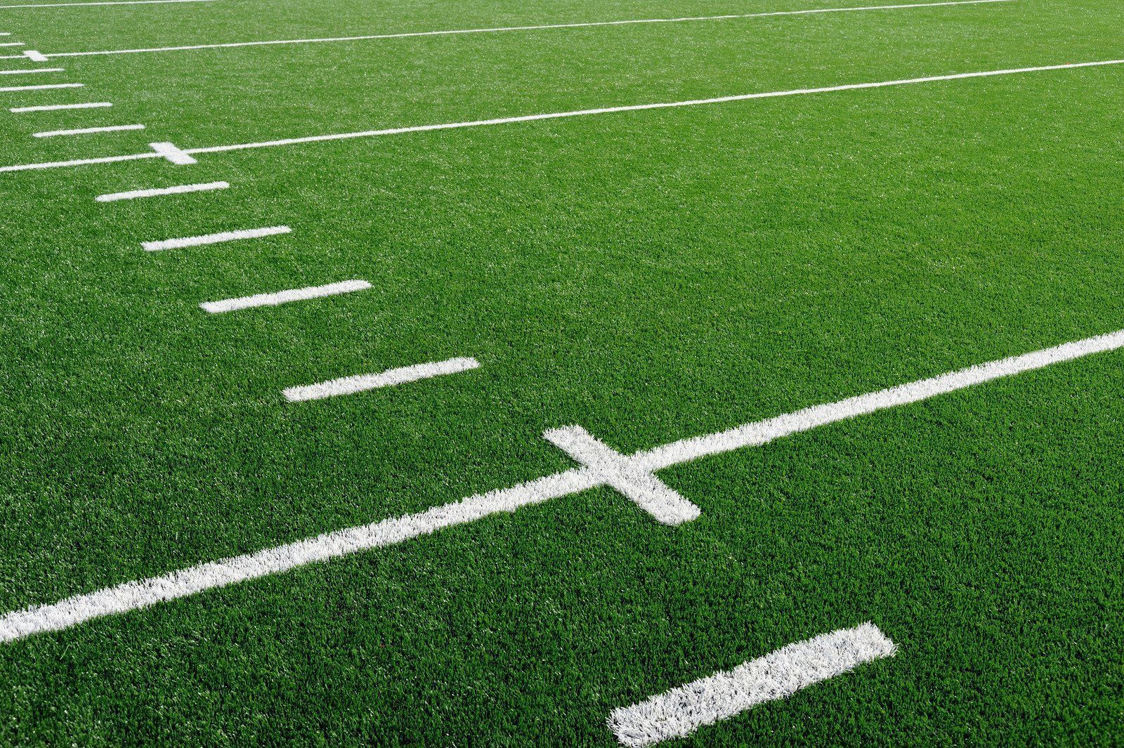 A high-angle view of a green artificial football field with white yard line markings.