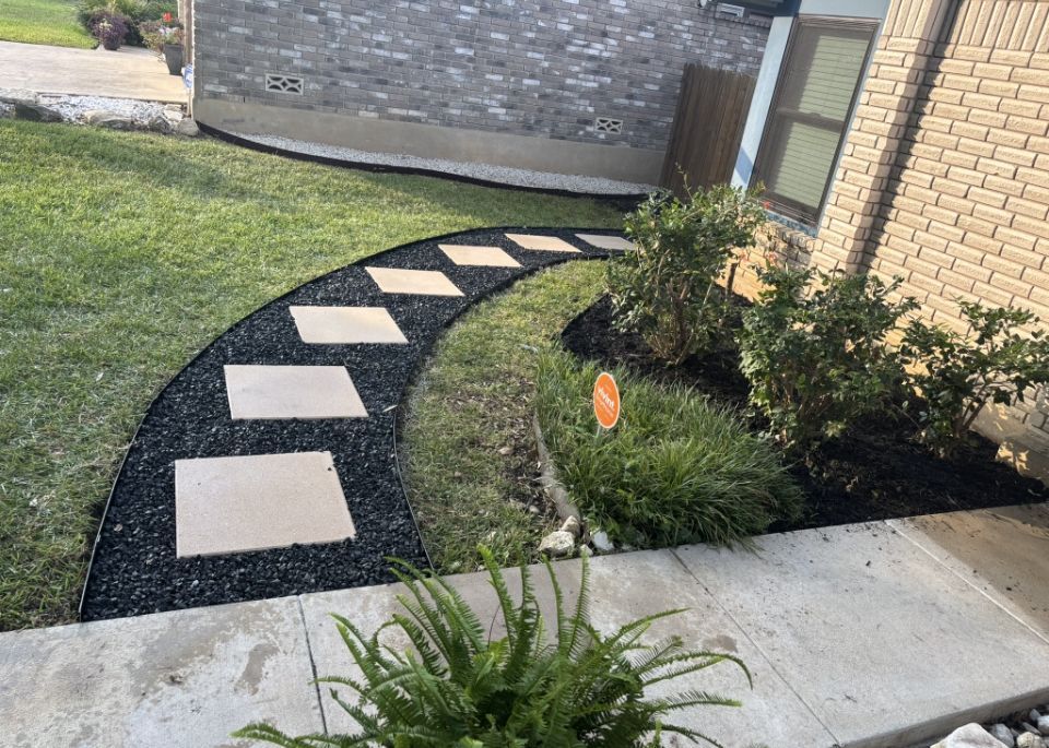 A curved stone paver walkway surrounded by black mulch, situated next to a brick house and green lawn.
