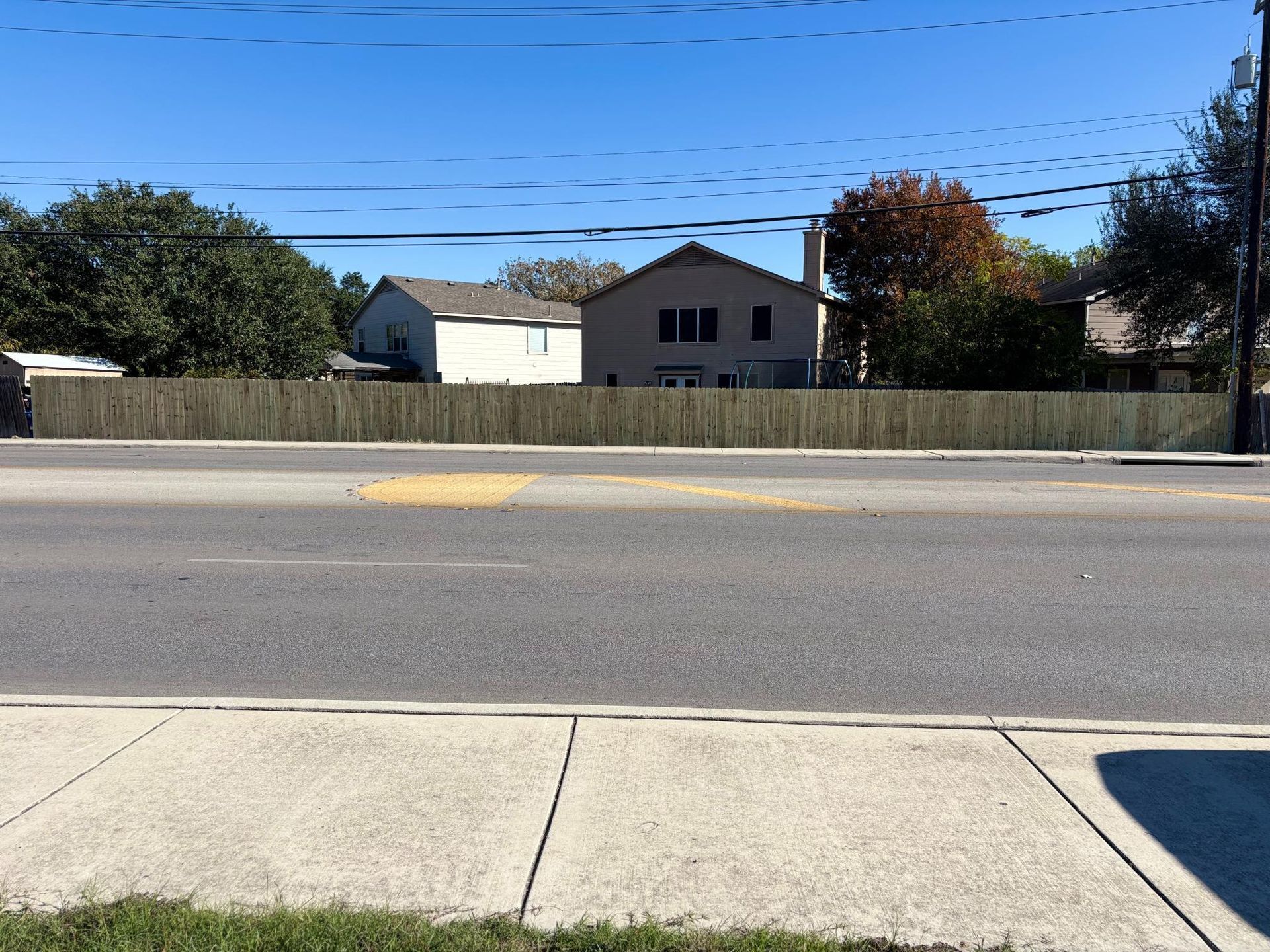 A street-level view of a wooden privacy fence in front of two residential houses under a clear blue sky.