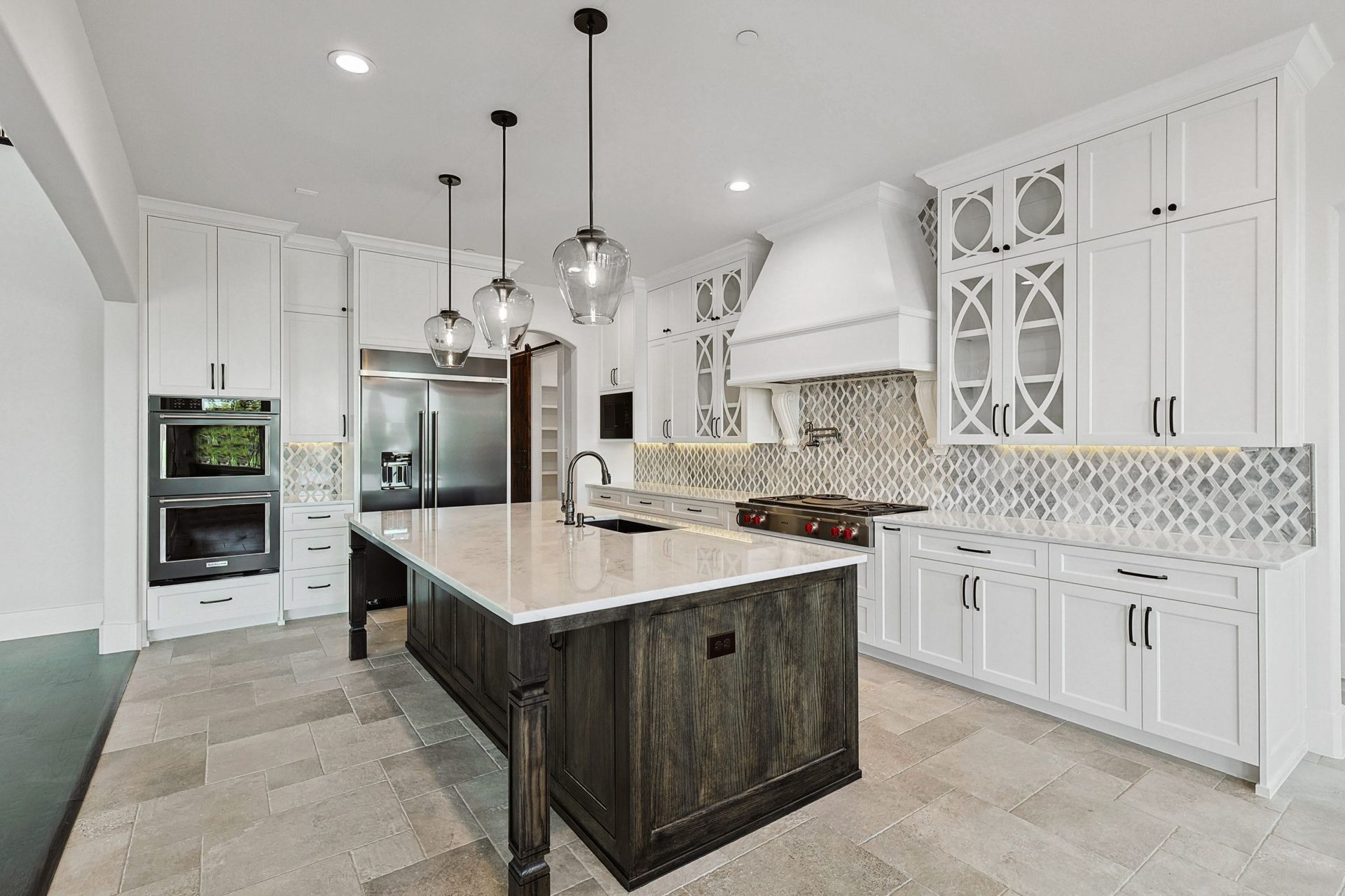 A spacious, modern kitchen featuring white cabinets, a large dark wood island with stone countertops, and tile flooring.