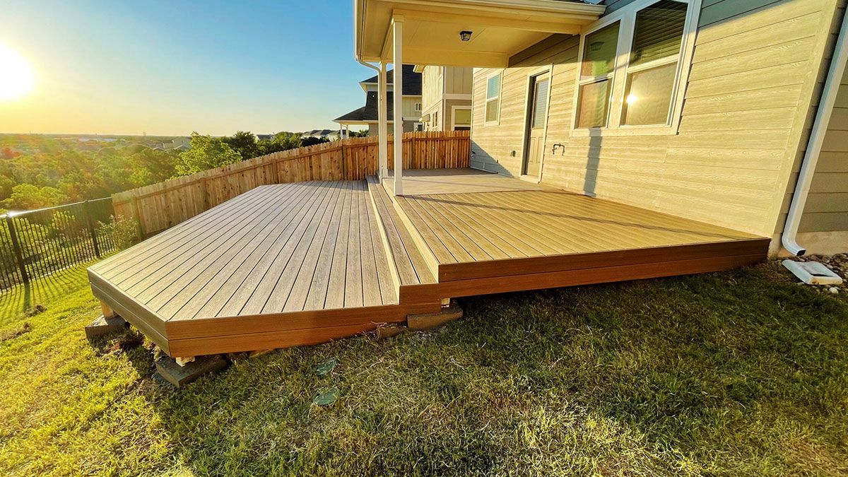 A two-level wooden deck attached to a house exterior, overlooking a grassy hill at sunset.