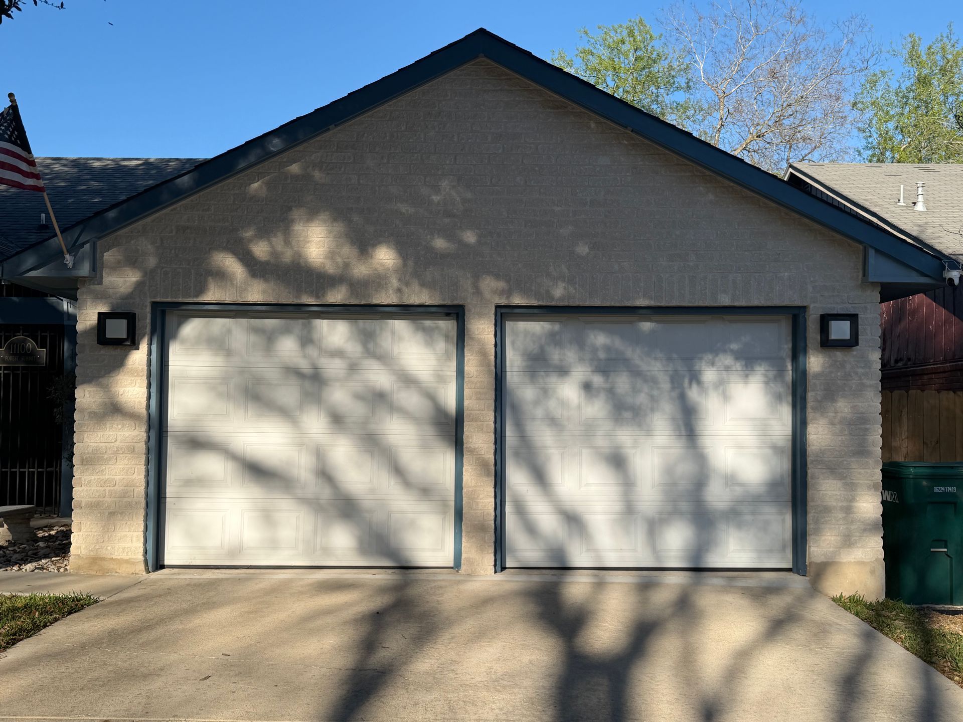 A two-car garage with white paneled doors, gray trim, and a concrete driveway in front of a house.