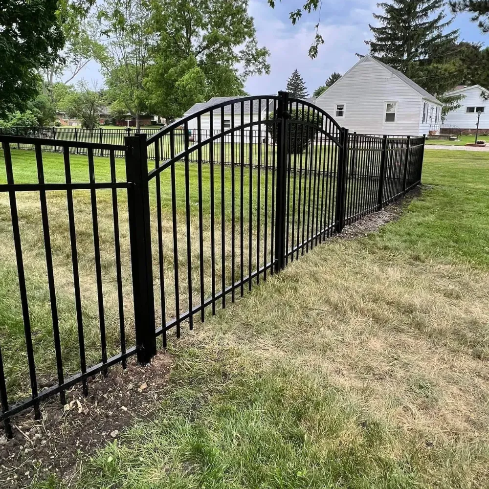 A black arched metal fence with vertical bars stands on a grassy lawn in front of a white house.