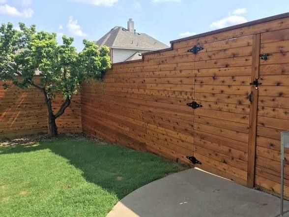 Wooden privacy fence with gate and small tree in yard.