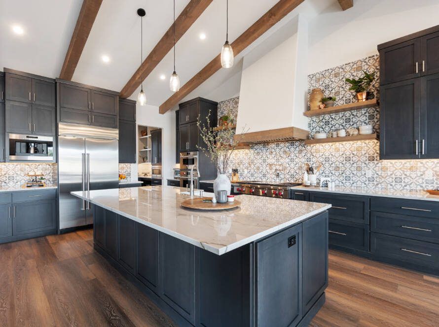 Modern kitchen with gray cabinets, large island, wood beams, and patterned tile backsplash.