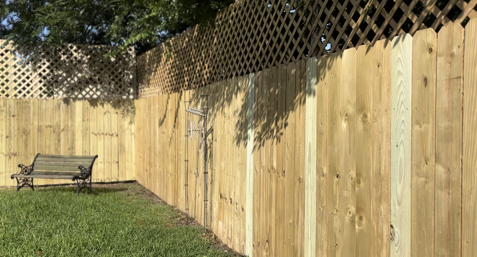 A wooden privacy fence with lattice topping in a backyard, featuring a small metal bench on green grass.