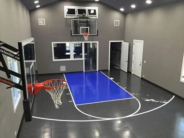 An indoor basketball court with gray walls, a blue key, and two basketball hoops.