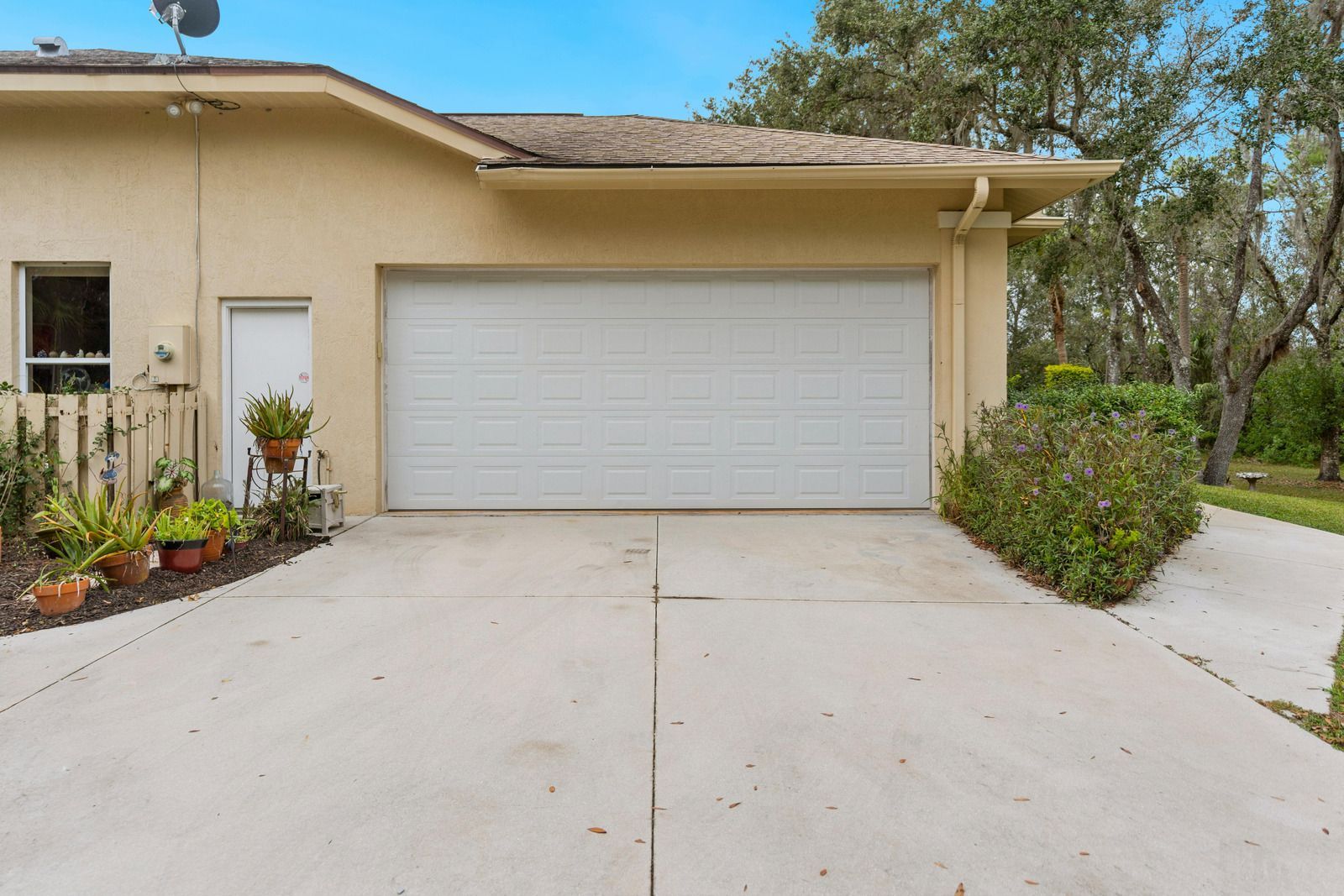 Garage of a beige house with a concrete driveway. Landscaping borders the house.
