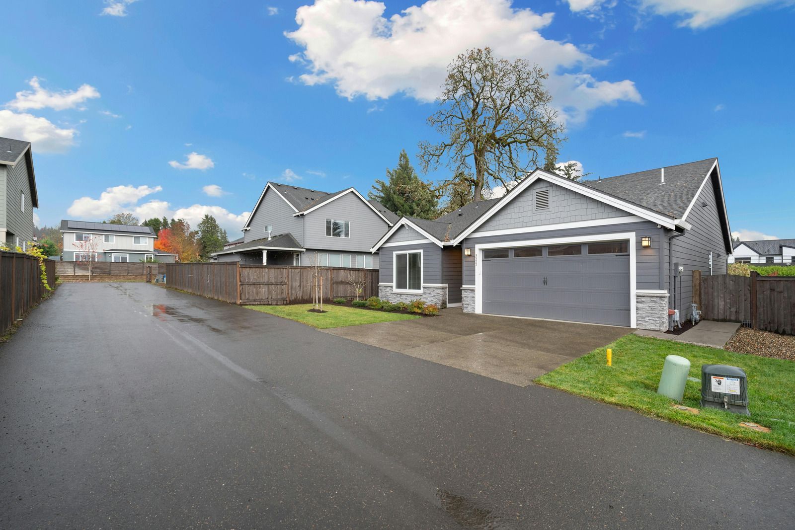 Gray house with a two-car garage on a wet street under a cloudy blue sky.