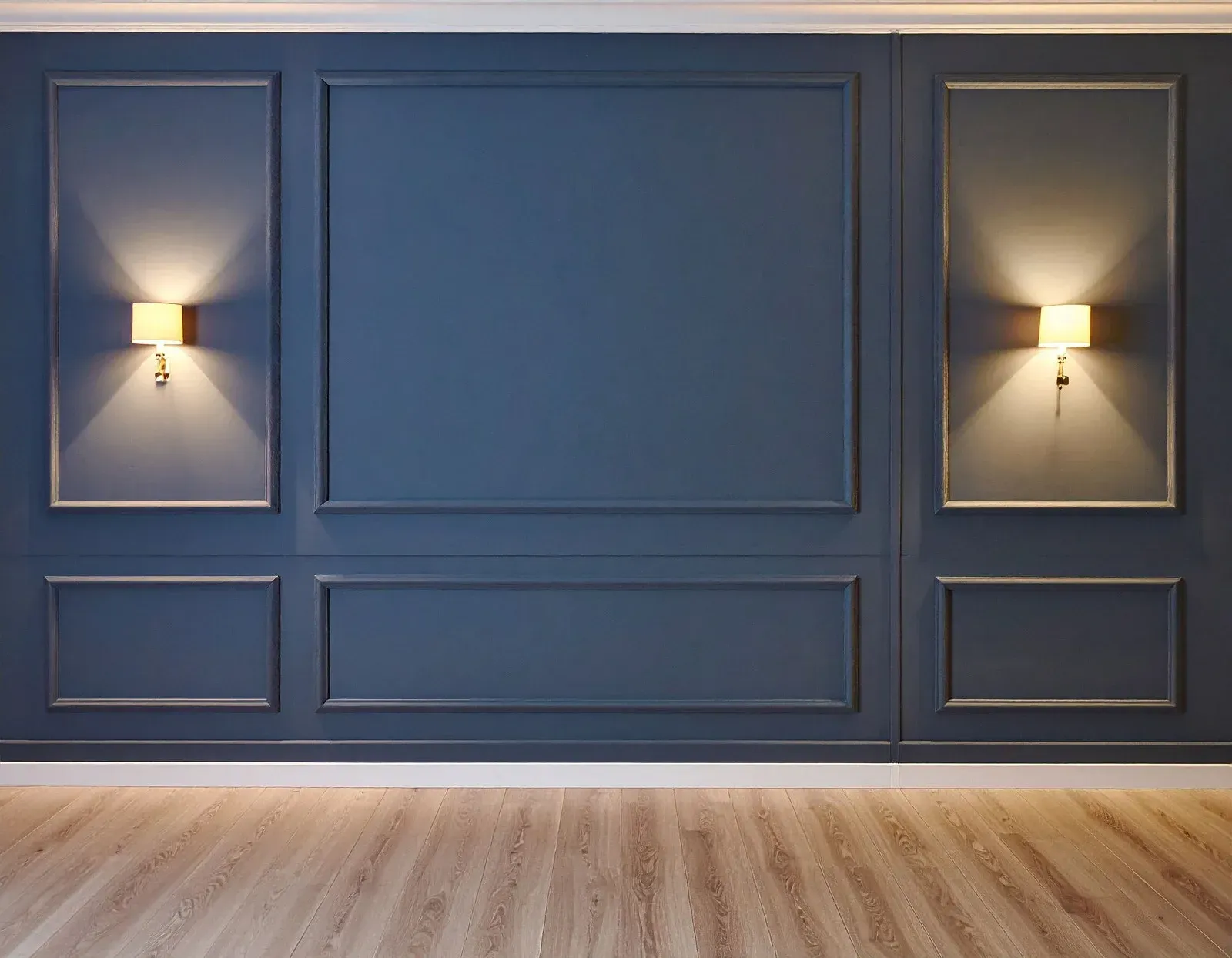 Man paints a blue wall, standing on plastic-covered floor, inside a room with exposed wood beams.