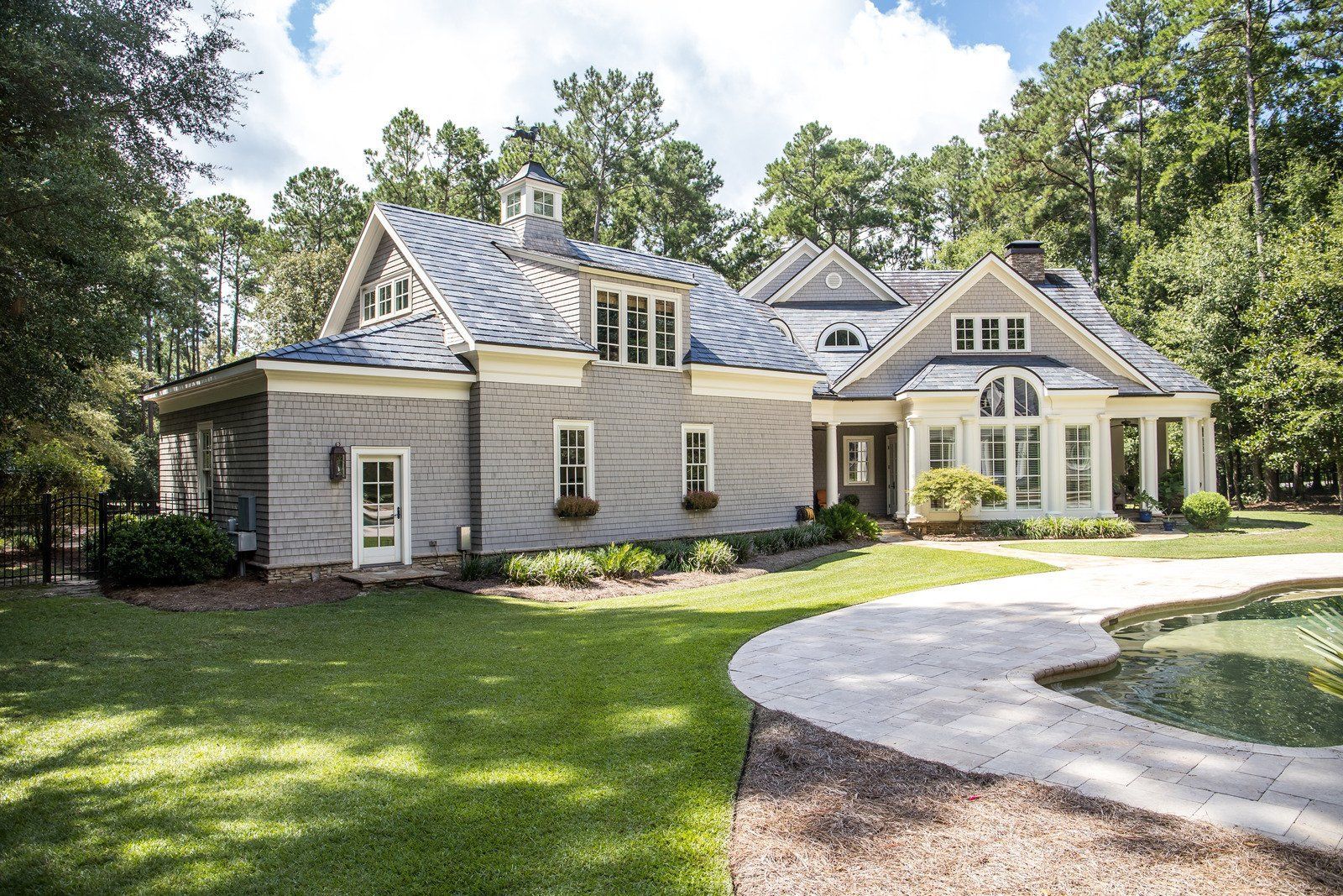 A large gray and white house with a curved driveway in a wooded area.