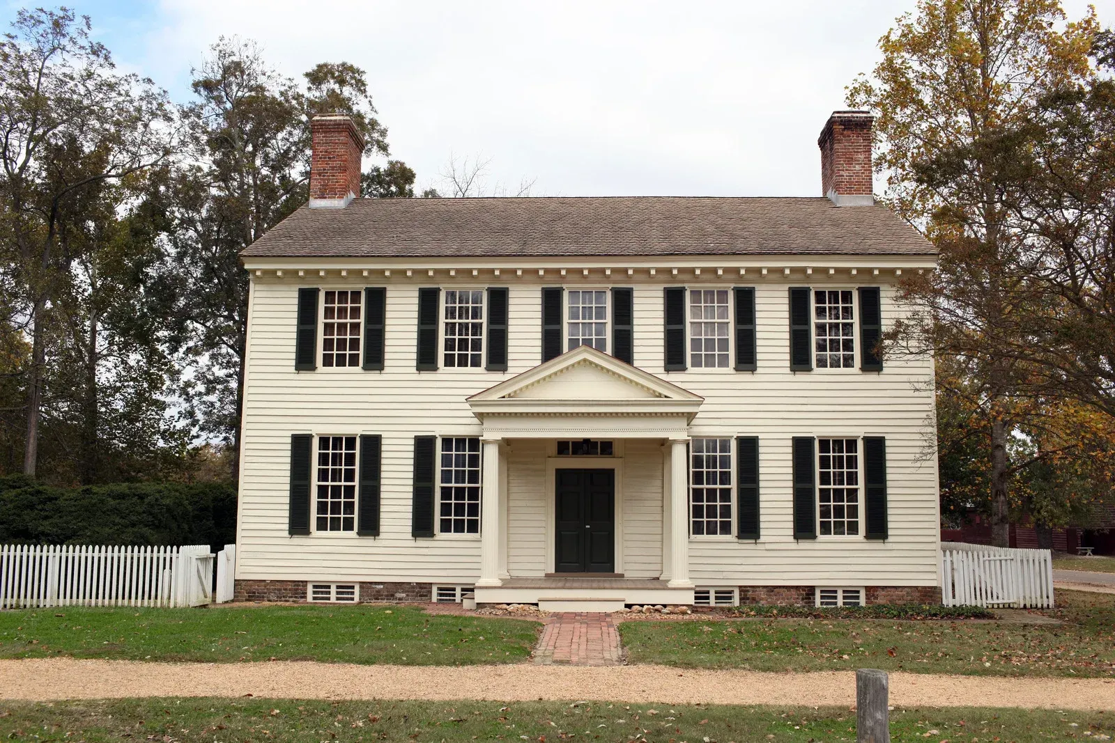 Two-story white house with black shutters and a small portico; brick path leading to the green door.