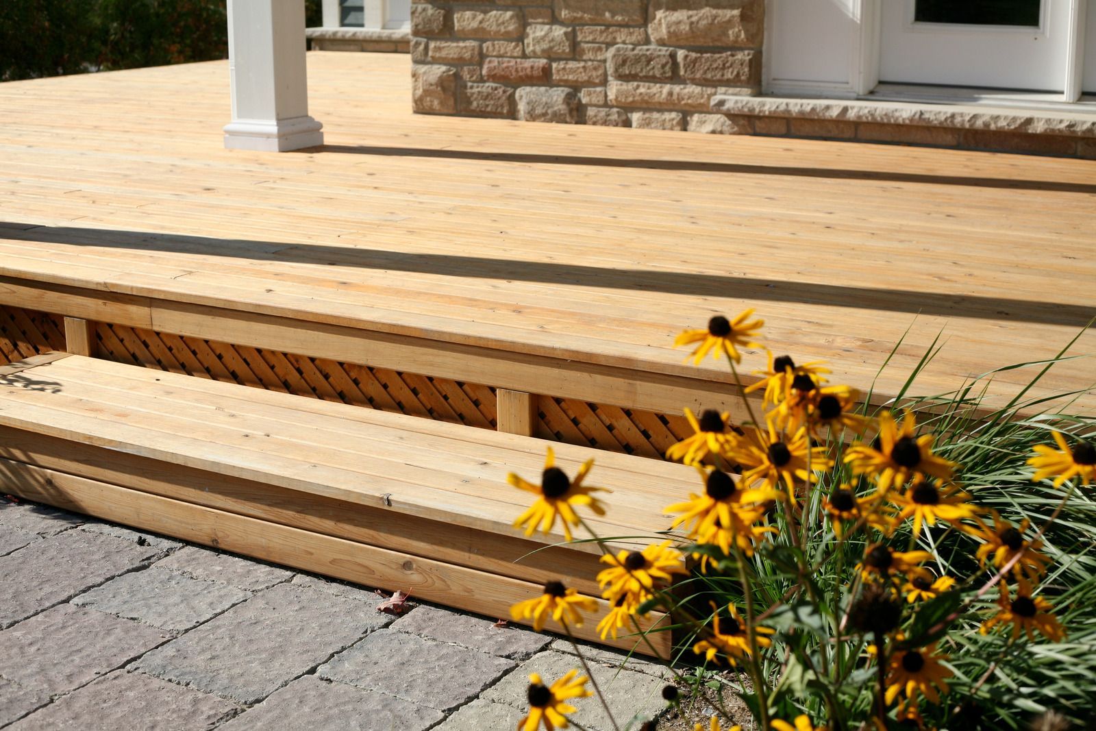 Wooden deck with steps, stone entrance, and yellow flowers.