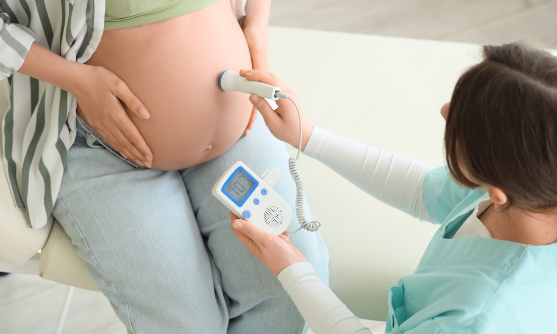 Pregnant woman having fetal heart rate checked with Doppler device.