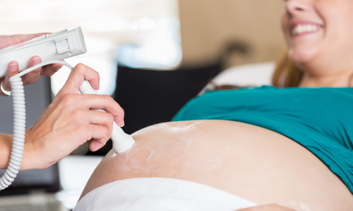 White baby booties with bear faces and ultrasound images on green leaves.