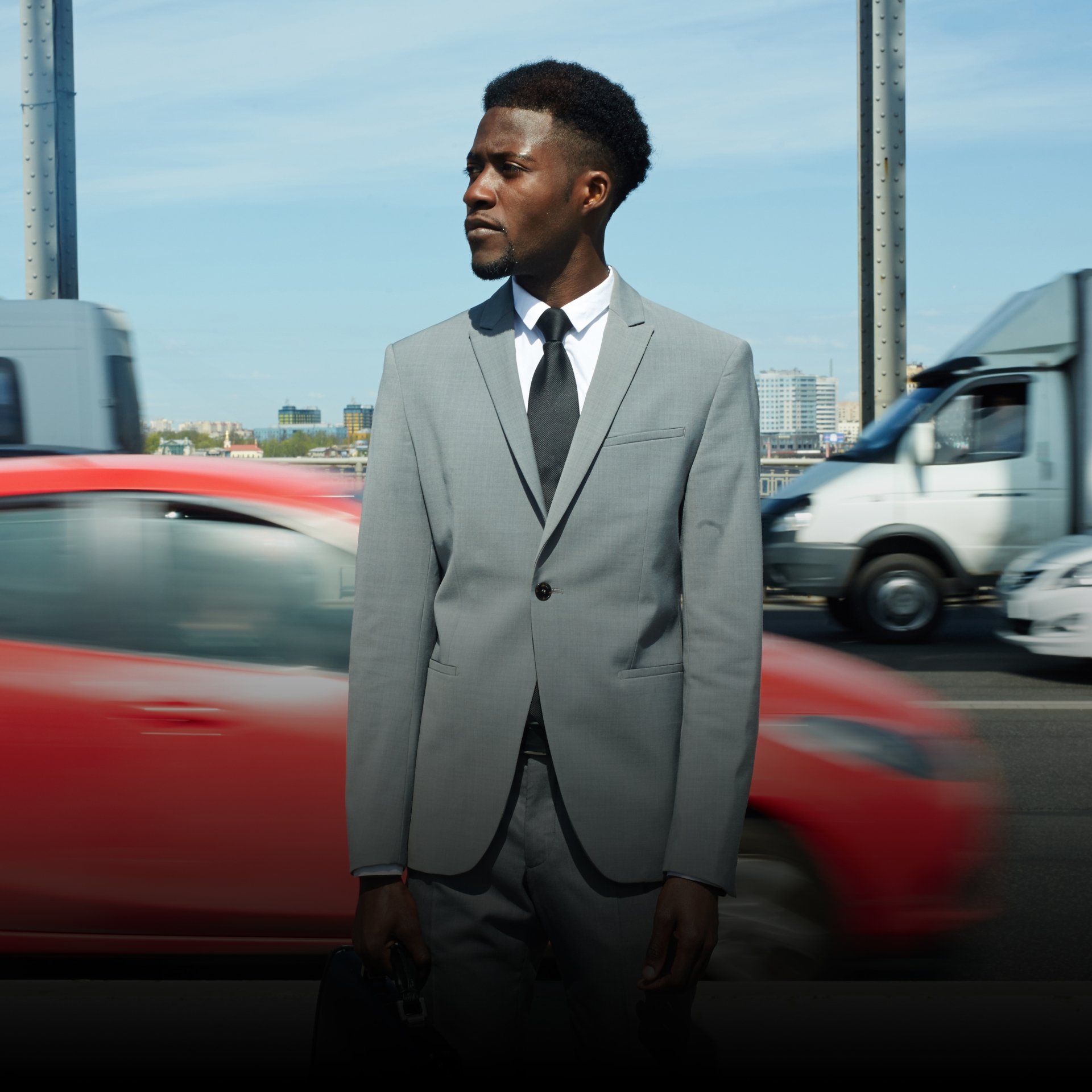 A man in a suit and tie is standing in front of a red car