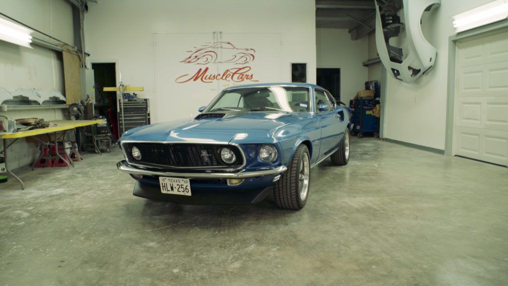 Blue classic car in a garage, with tools and car parts visible.