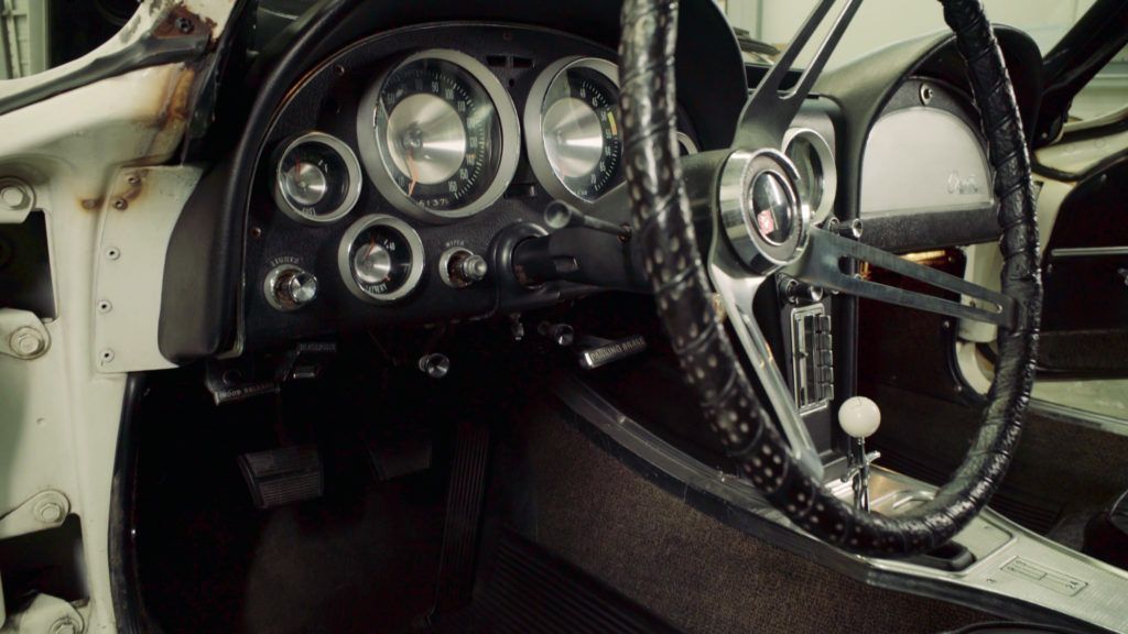 Black and silver car dashboard with gauges, steering wheel, and gear shift, inside a white car.