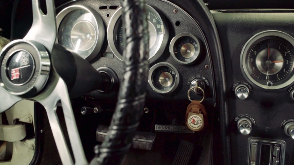 Dashboard and steering wheel of a classic black car, gauges, and keys visible.