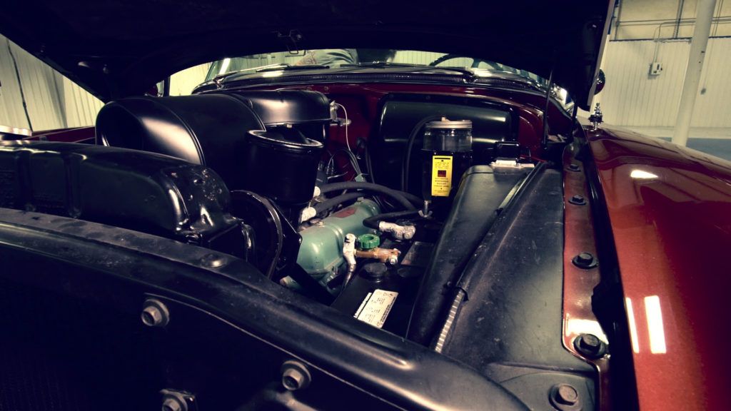 Open hood of a classic red car, revealing the engine compartment.