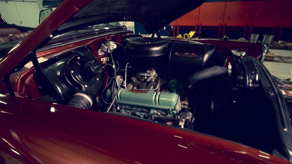Red classic car with its hood up, showcasing a teal engine bay.