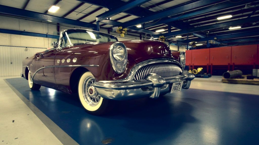 Burgundy classic convertible car parked indoors with blue floor, white wall tires.