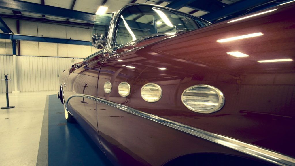 Maroon classic car with side lights on display inside a building.