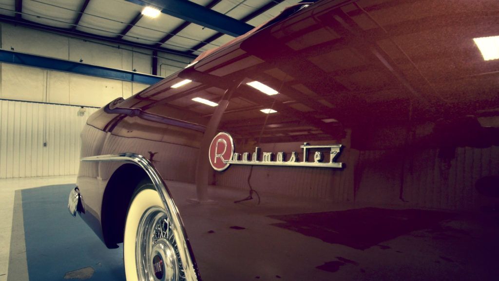 Burgundy-colored 1950s Packard Caribbean classic car with chrome details inside a garage.