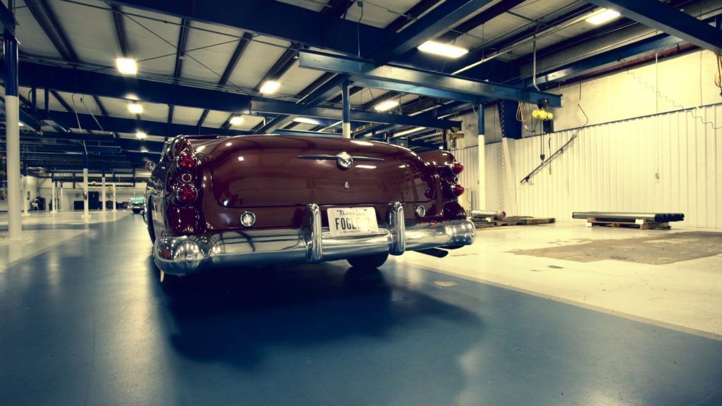 A classic burgundy car parked inside a large, industrial garage.