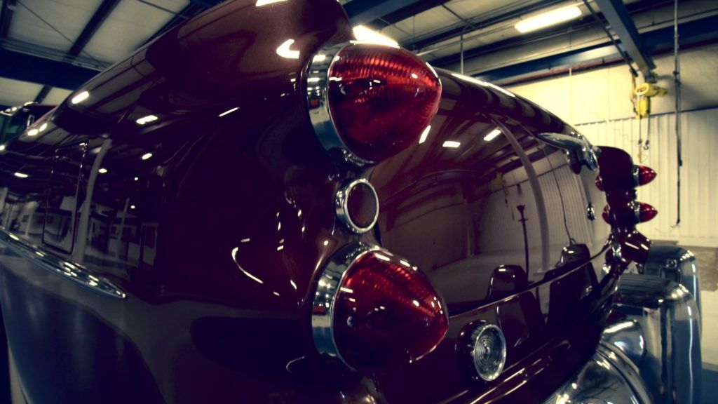 Shiny maroon classic car with chrome lights in an industrial setting.
