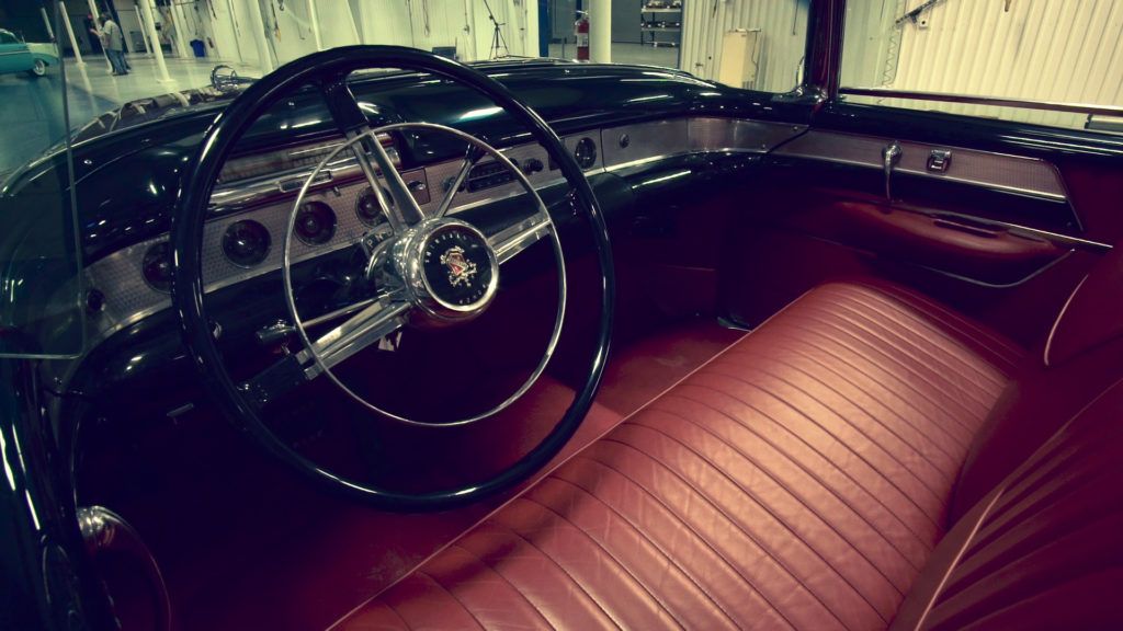 Interior of a classic black convertible car with red leather seats and chrome details.
