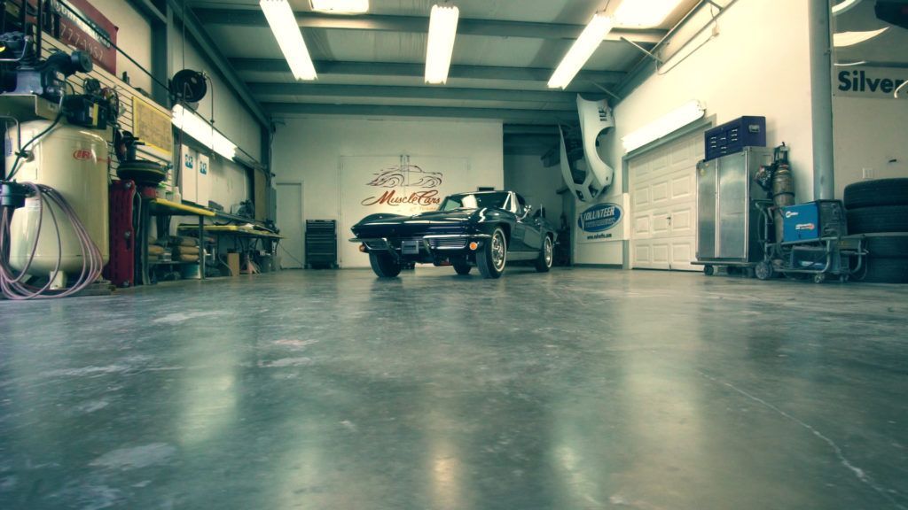 Classic black car inside a garage with tools and equipment; a well-lit workspace.