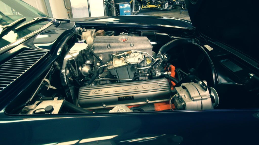 Engine of a classic car with the hood open, showing chrome details and a silver engine block.