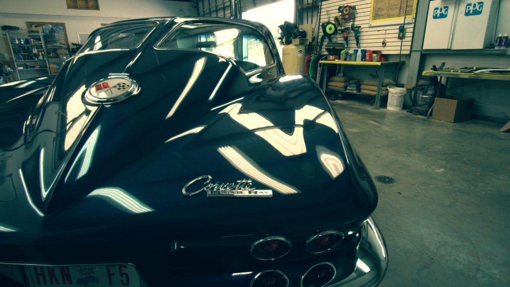 Dark blue classic Corvette in a garage, shiny finish, chrome details, license plate.