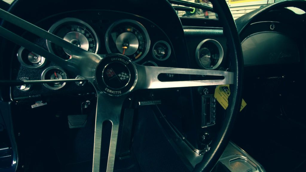 Dashboard and steering wheel of a classic black Corvette with silver accents.