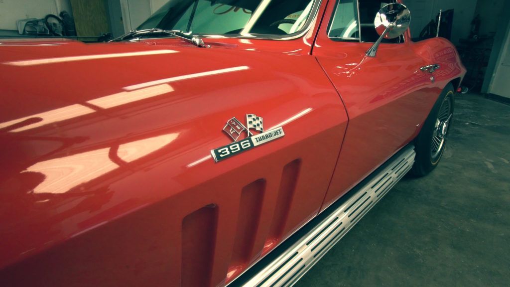 Red vintage Chevrolet Corvette. Chrome emblems, side pipe, and bright red paint.
