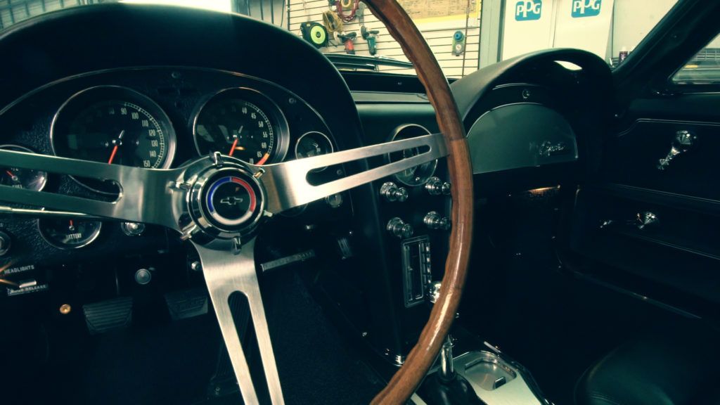 Black classic car interior with wooden steering wheel and chrome details.