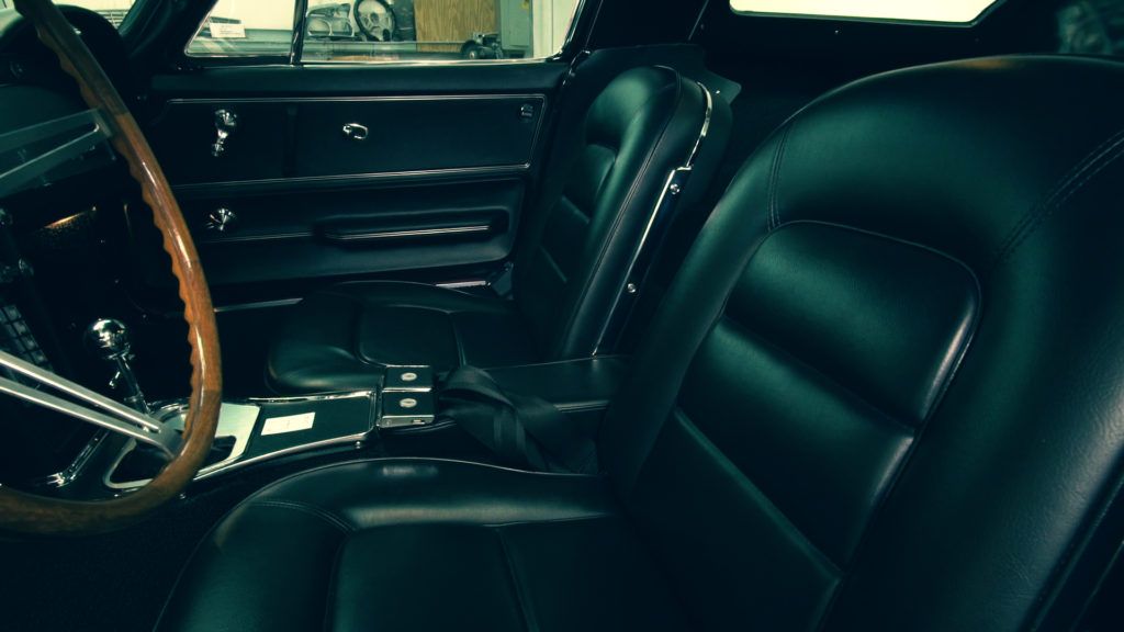 Black leather car interior with wooden steering wheel, dashboard, and seats.