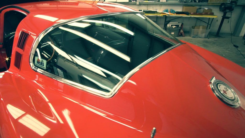 Red classic Corvette's rear window and roof, with chrome trim. Interior visible, likely in a garage.