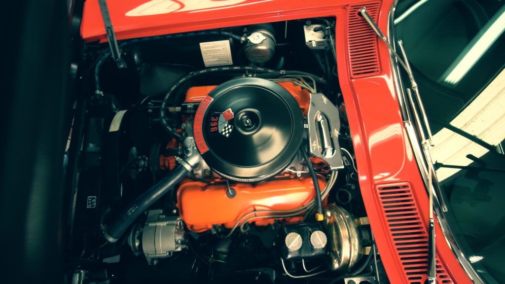 Red classic car engine bay; orange engine block, black air cleaner, chrome components.