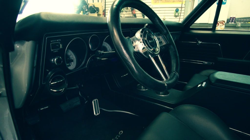 Classic car interior: black leather seats, chrome steering wheel, dashboard with gauges.