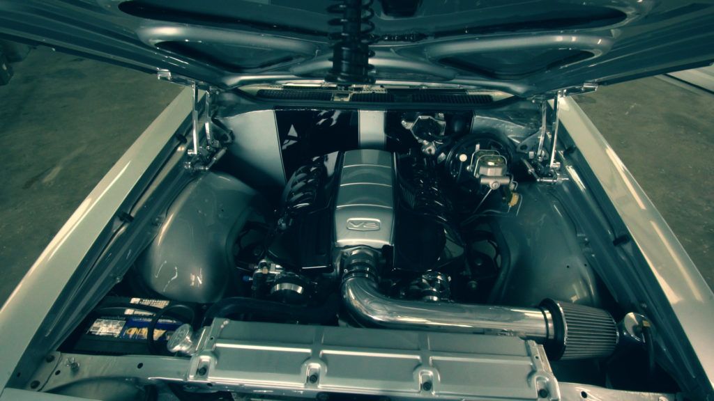 Engine of a classic car, silver and black, hood open.