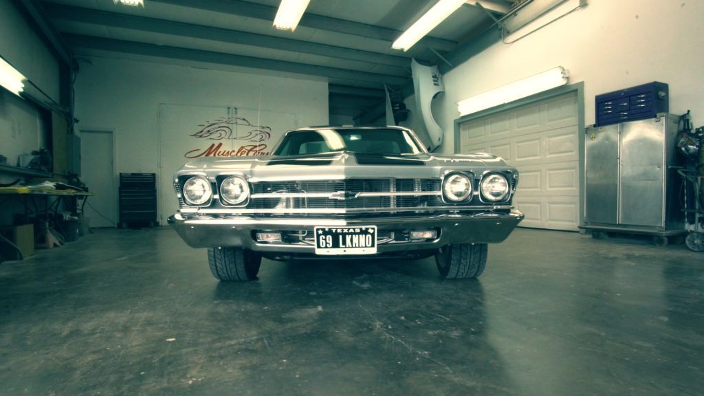Classic silver car in a garage, headlights on.