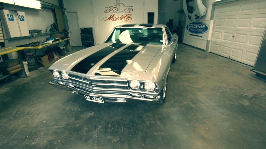 Silver classic car with black racing stripes inside a garage.