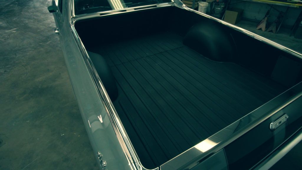 Grey classic car truck bed with a black liner, indoors.