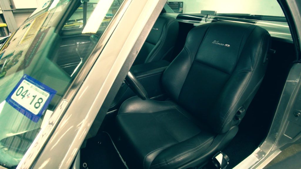 Black leather car seat inside a classic car. April 2018 license plate visible.