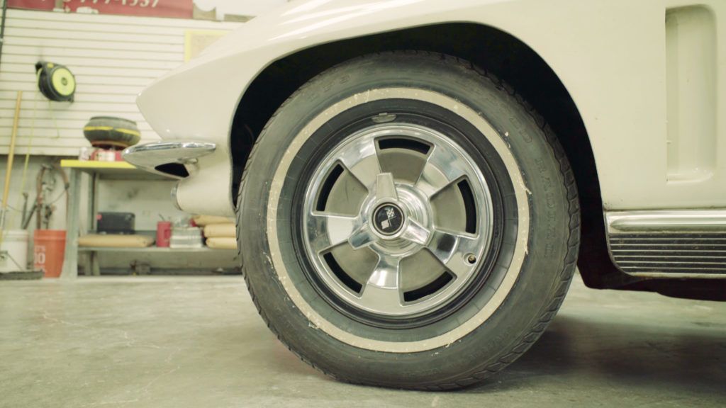 White classic car, front wheel with chrome hubcap, in a garage.