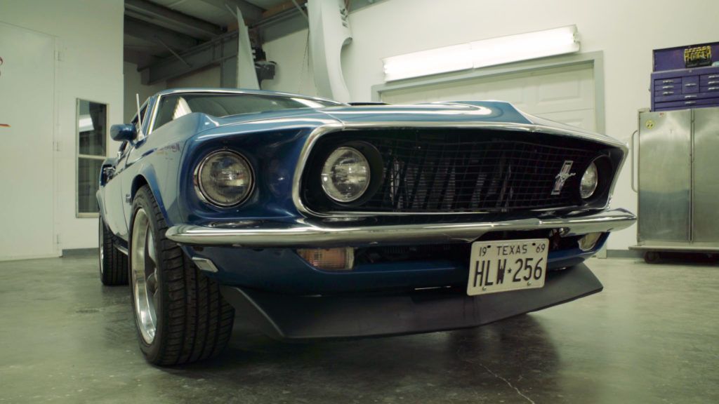 Blue vintage Ford Mustang in a garage, low angle.